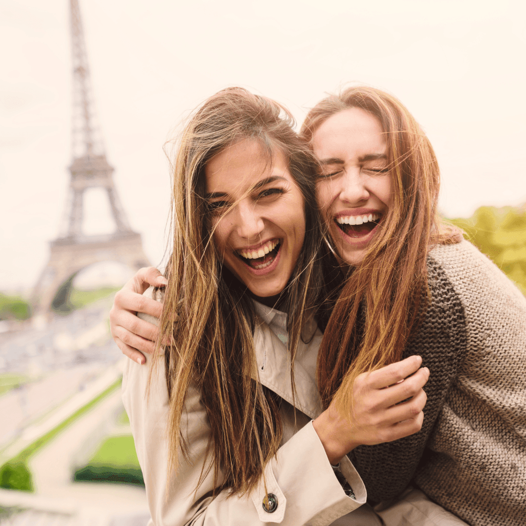 Two women laughing and embracing with the Eiffel Tower in the background.