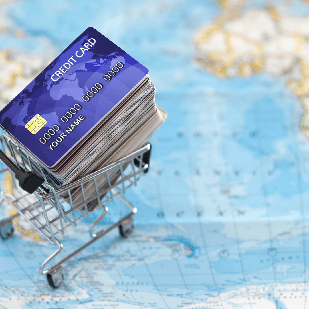 Small shopping cart filled with stacked credit cards placed on a world map background.